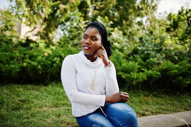 Chica musulmana africana con sudadera blanca hiyab negra y jeans sentada al aire libre