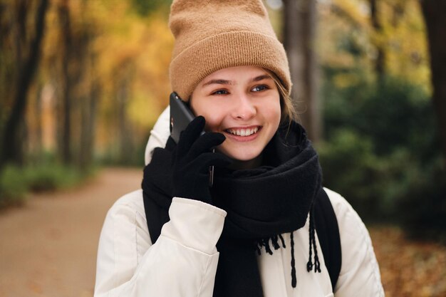 Chica muy alegre felizmente hablando por teléfono celular caminando en el parque de otoño