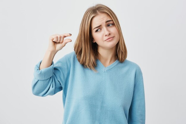 Chica muy linda con ropa casual mostrando algo pequeño en tamaño con las manos mientras gesticula, frunciendo el ceño