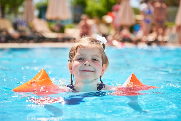 Chica nadando en la piscina en brazaletes en un caluroso día de verano. Vacaciones familiares en un resort tropical
