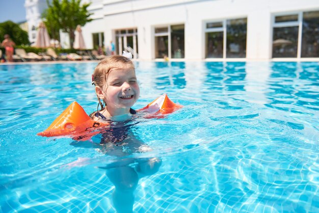 Chica nadando en la piscina en brazaletes en un caluroso día de verano. Vacaciones familiares en un resort tropical