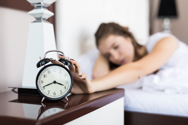 Chica de negocios estudiante cansado se despierta por la mañana debido al despertador que suena en el dormitorio