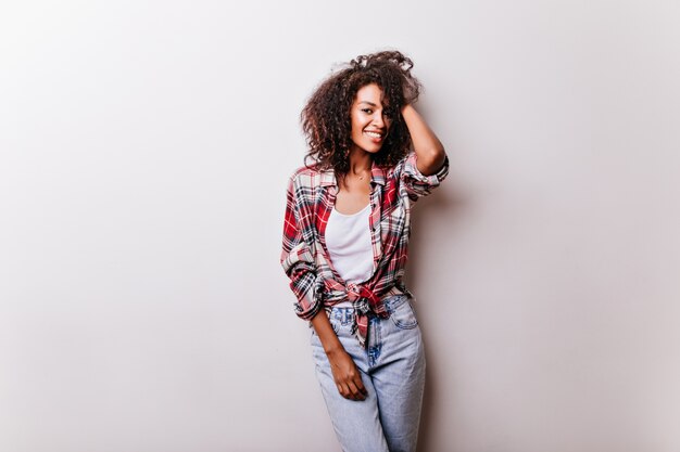 Chica negra delgada en traje de moda posando con disfrute. Señora africana de pelo corto de pie sobre blanco.