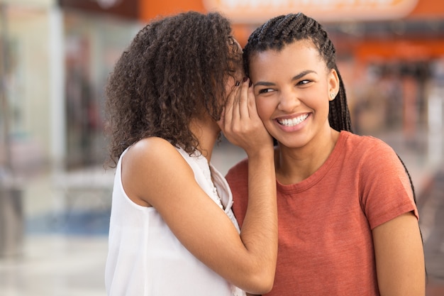 Chica negra que susurra secreto a la novia sonriente