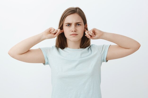 Chica no va a escuchar cerrando los oídos. Mujer molesta de aspecto serio intenso cubriendo la audición con los dedos índices y de pie indiferente y no involucrada no dispuesta a continuar la conversación