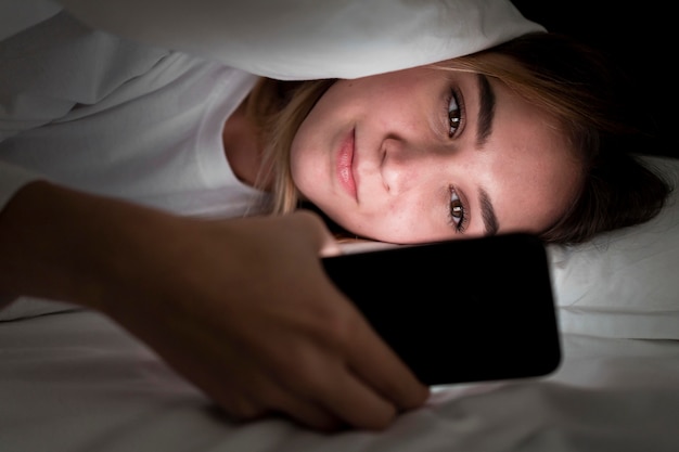 Foto gratuita chica de noche en la cama con teléfono de cerca