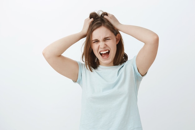 La chica odia pensar demasiado. Mujer europea molesta joven angustiada disgustada con corte de pelo corto marrón gritando mientras pierde los estribos estando enojado o enojado arruinando o tirando el cabello de la cabeza