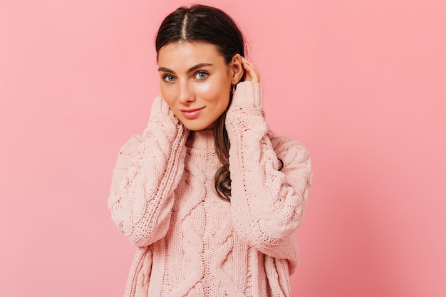 Foto gratuita chica de ojos azules sin maquillaje mira a cámara. retrato de mujer en suéter de punto sobre fondo rosa.