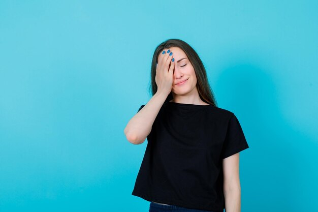 Chica de ojos cerrados está poniendo la mano en el ojo sobre fondo azul.