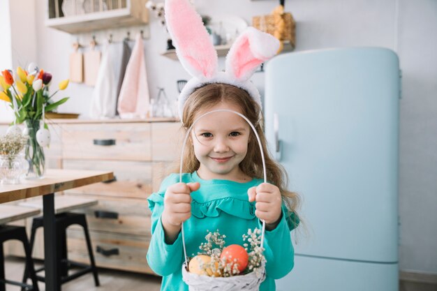 Chica en orejas de conejo con canasta con huevos de Pascua