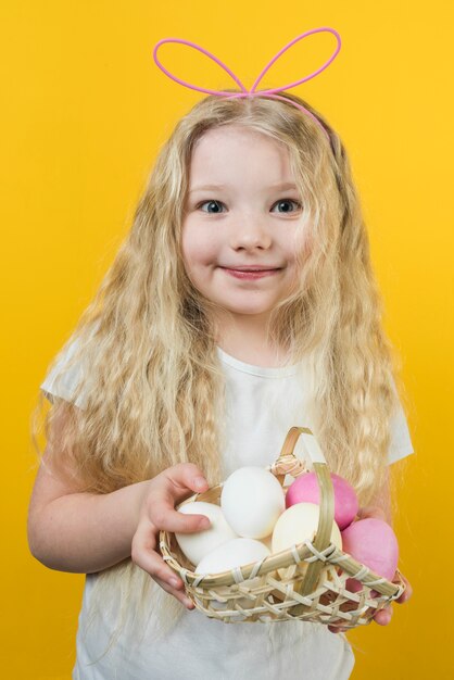 Chica en orejas de conejo con canasta con huevos de Pascua