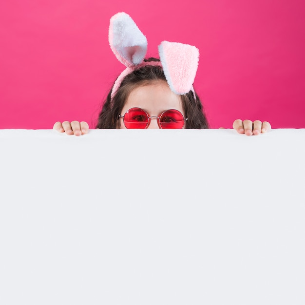 Foto gratuita chica con orejas de conejo y gafas de sol escondidas detrás de la mesa