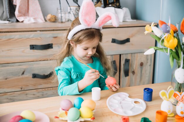 Chica en orejas de conejo pintando huevos para Pascua