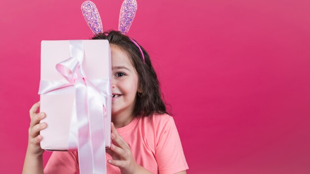 Chica en orejas de conejo que cubre la cara con caja de regalo