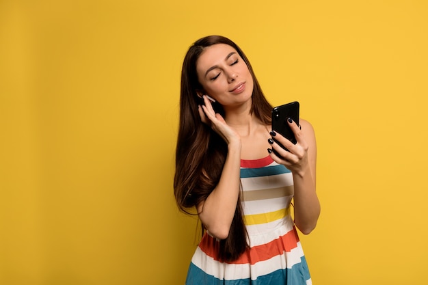 Chica pacificada con los ojos cerrados escuchando música en auriculares con un vestido brillante