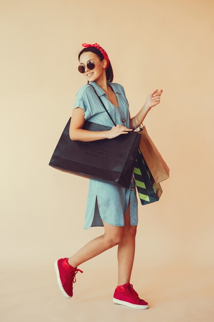 Chica en una pared amarilla con bolsas de compras