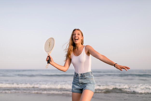 Chica en la parte superior del tanque y pantalones cortos jugando al tenis en la orilla del mar