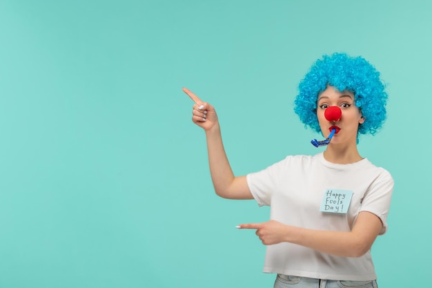 Chica de payaso del día de los inocentes silbar ambas manos apuntando a la izquierda gafas de sol azules traje divertido cabello azul