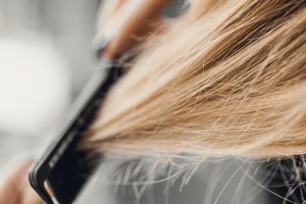 Chica peinando el cabello rubio con un cepillo. De cerca