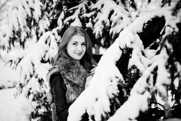 Chica pelirroja con abrigo de piel caminando en el parque nevado de invierno