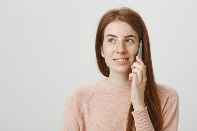 Chica pelirroja alegre con pecas, sonriendo y hablando por teléfono sin preocupaciones