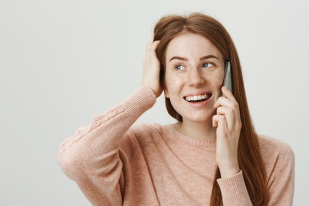 Chica pelirroja atractiva feliz riendo mientras habla por teléfono, conversando