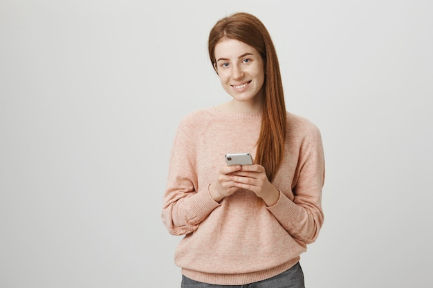 Chica pelirroja atractiva con smartphone y sonriendo