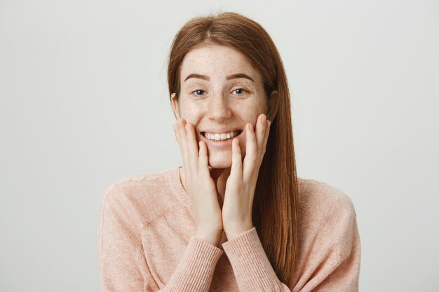 La chica pelirroja emocionada se ve halagada o conmovida, sonriendo sorprendida