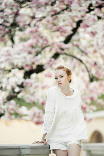 Foto gratuita chica pelirroja se encuentra en el árbol de flor rosa