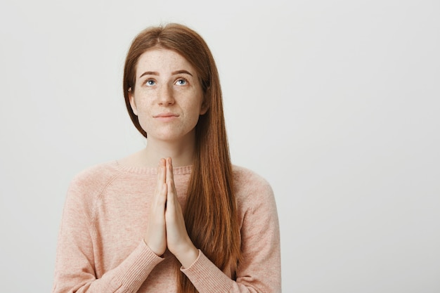 Chica pelirroja esperanzada suplicando a Dios, tomados de la mano en una oración y mirando hacia arriba