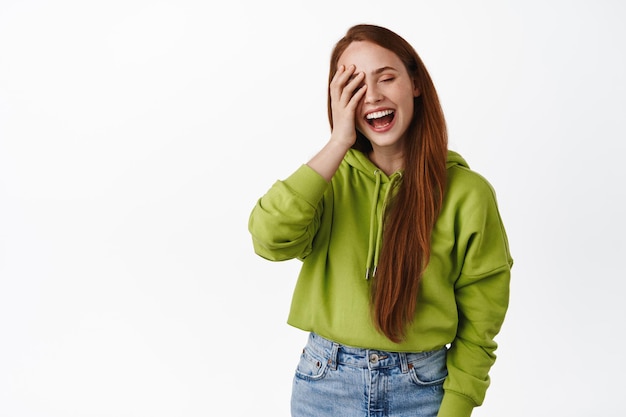 Foto gratuita chica pelirroja feliz riendo y sonriendo, sosteniendo la mano en la cara sin maquillaje, fondo blanco.