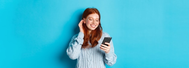 Foto gratuita chica pelirroja feliz de tecnología mirando complacida con el cumplido de lectura de teléfono móvil en el mensaje sonriendo