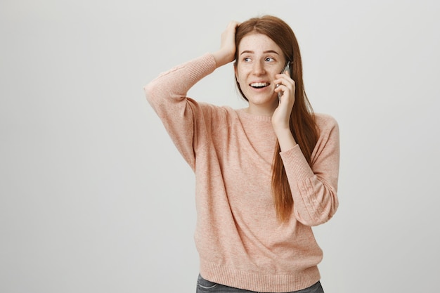 Chica pelirroja linda sorprendida hablando por teléfono y sonriendo