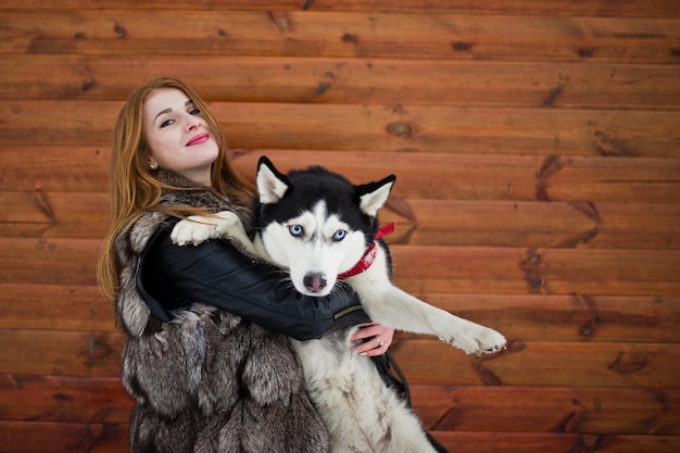 Chica pelirroja con perro husky contra la pared de madera