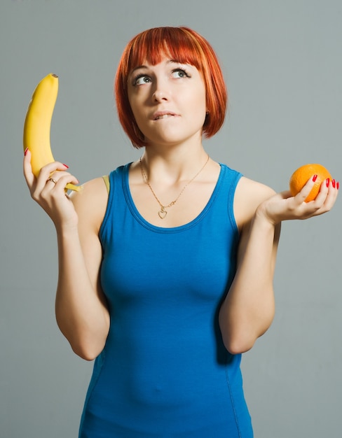 Chica pelirroja con plátano y naranja