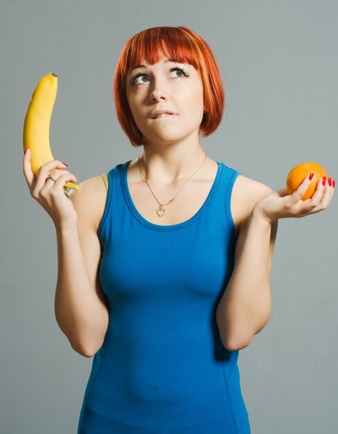 Chica pelirroja con plátano y naranja