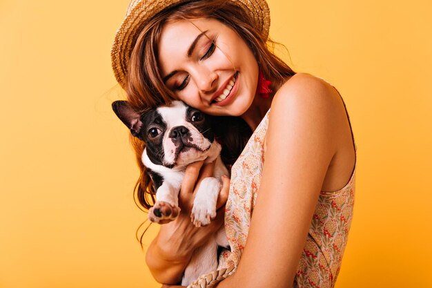 Chica pelirroja relajada abrazando cachorro sobre fondo amarillo Retrato de estudio de mujer blanca atractiva relajándose con perro