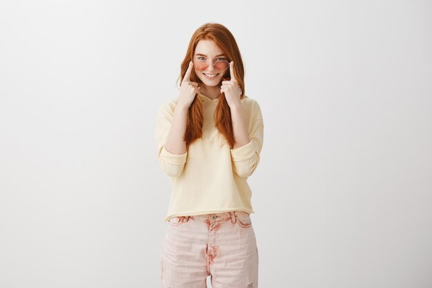 Chica pelirroja sonriente mostrando gafas de sol nuevas