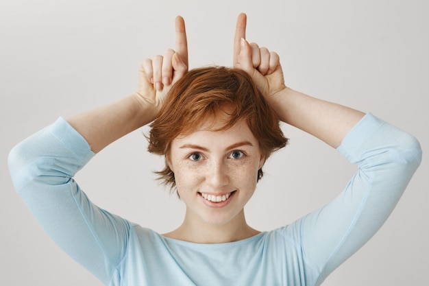 Foto gratuita chica pelirroja sonriente posando contra la pared blanca