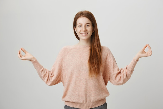 Chica pelirroja tranquila pacífica meditando, levanta las manos en gesto zen