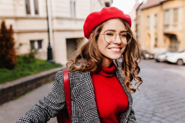 Chica de pelo castaño inspirada con expresión de cara feliz cruza la calle en un día cálido