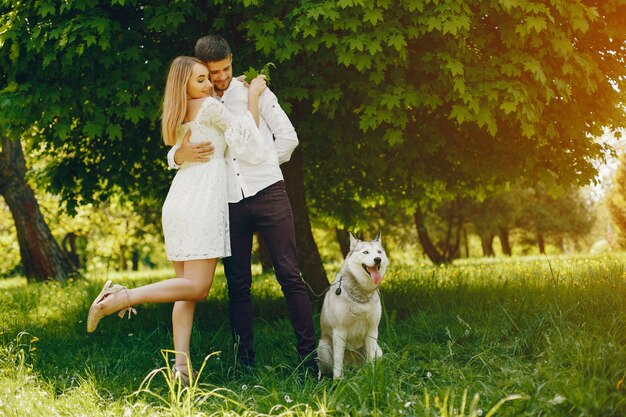 chica con pelo claro y un vestido blanco en un bosque soleado con su novio y perro