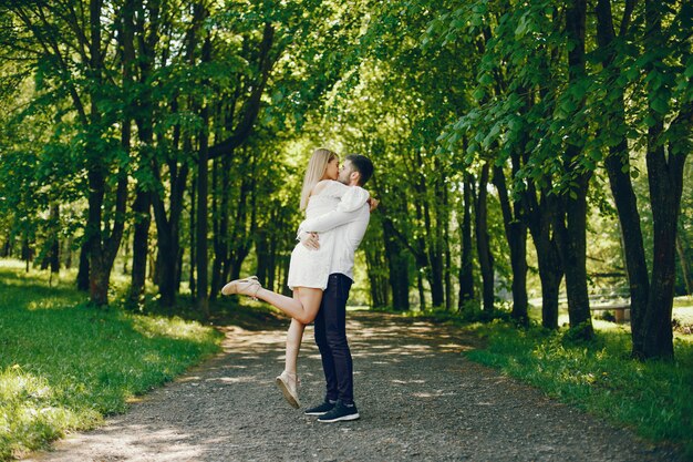 chica con pelo claro y un vestido blanco está caminando en un bosque soleado con su novio