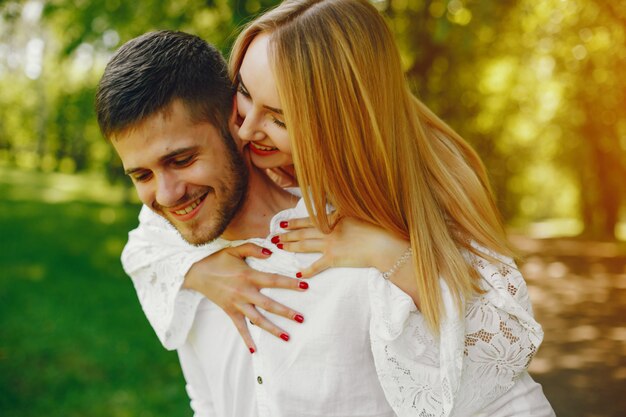 chica con pelo claro y un vestido blanco está caminando en un bosque soleado con su novio