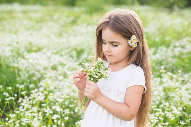 Chica con el pelo largo mirando flores blancas recogidas por ella en el campo