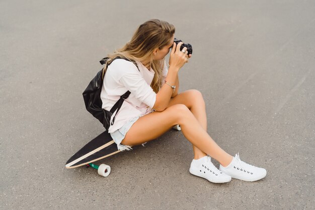 chica con el pelo largo con monopatín fotografiando en cámara. calle, deportes activos