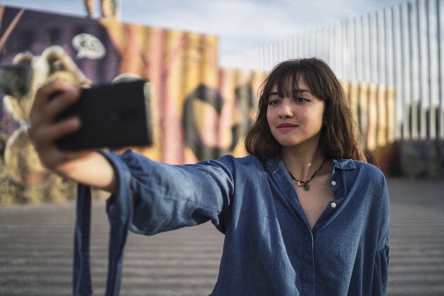 Chica de pelo negro tomando una foto de sí misma detrás de un edificio