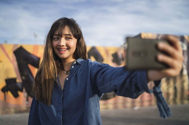 Chica de pelo negro tomando una foto de sí misma detrás de un edificio