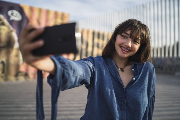 Chica de pelo negro tomando una foto de sí misma detrás de un edificio