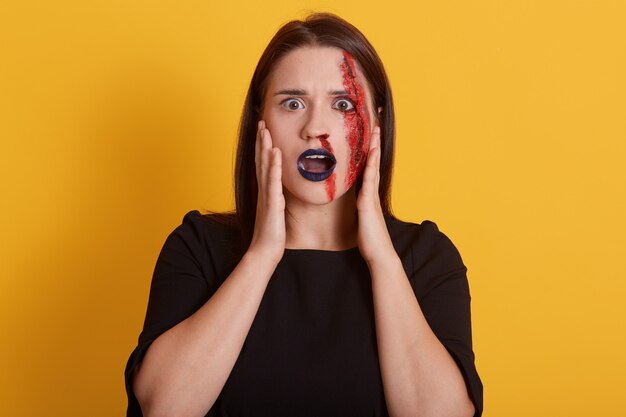 Chica con el pelo oscuro y liso, con una herida ensangrentada en la cara, ojos grandes llenos de miedo, mantiene la boca ligeramente abierta, ve vampiros, asesinos o psicópatas frente a ella, concepto de Halloween.